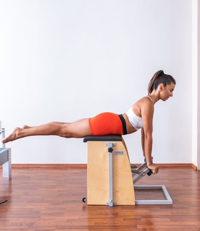 A woman performs a Pilates exercise on a Wunda chair, showcasing strength and balance.